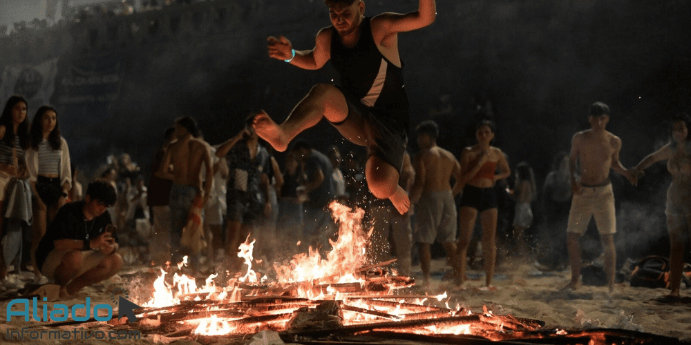 Hogueras de la noche de San Juan en la playa con personas saltando sobre el fuego durante la celebración